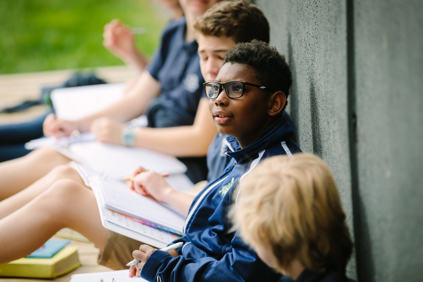 kids sitting by an outside wall with open books